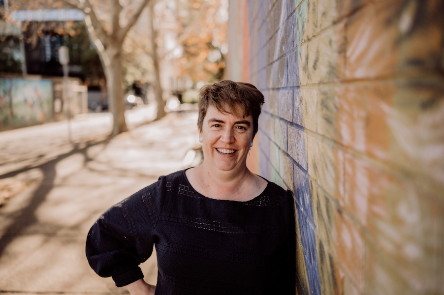 A photo of Rachel Amies wearing a dark blue top, leaning against a colourful wall and smiling at the camera. It's the main image for her website design services page on her website.