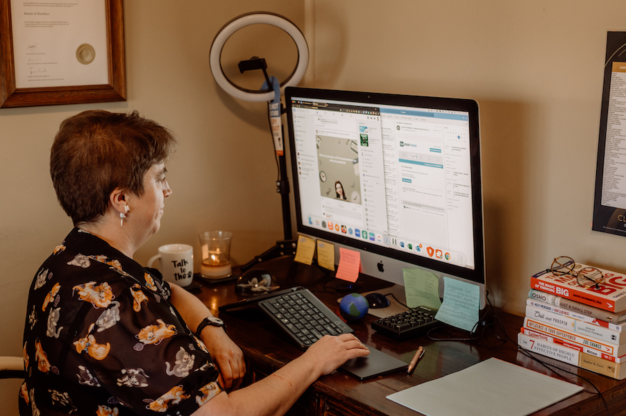 Image of Rachel Amies wearing a black shirt with white and ginger cats. She's sitting at a desk with a desktop computer. This is the hero image for her WordPress support Australia services.